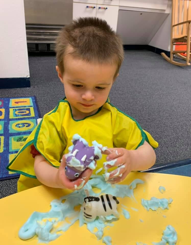 Child playing with toys and blue foam at a yellow table