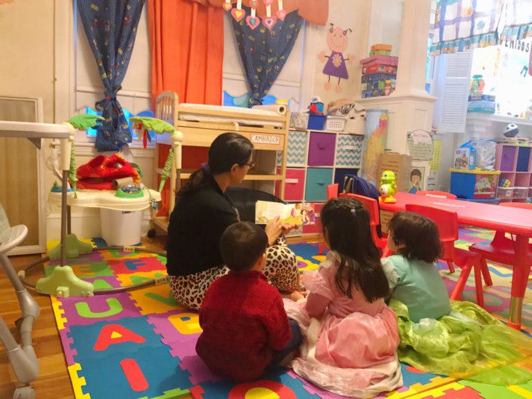 Person reading a book to three children in a classroom