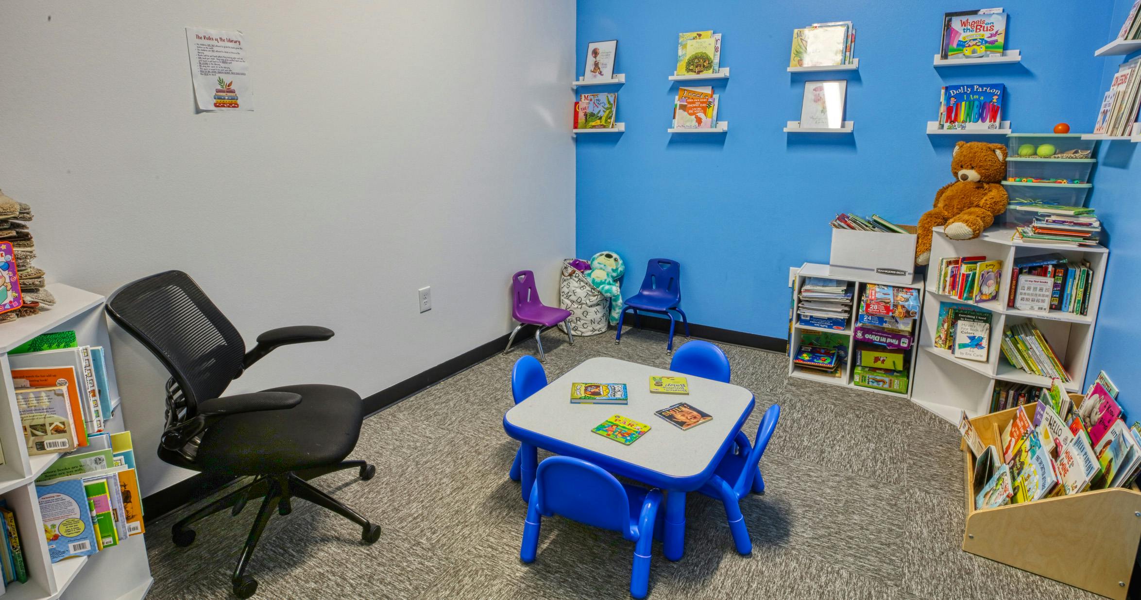 Children's corner with small table and chairs, bookshelves, and a teddy bear