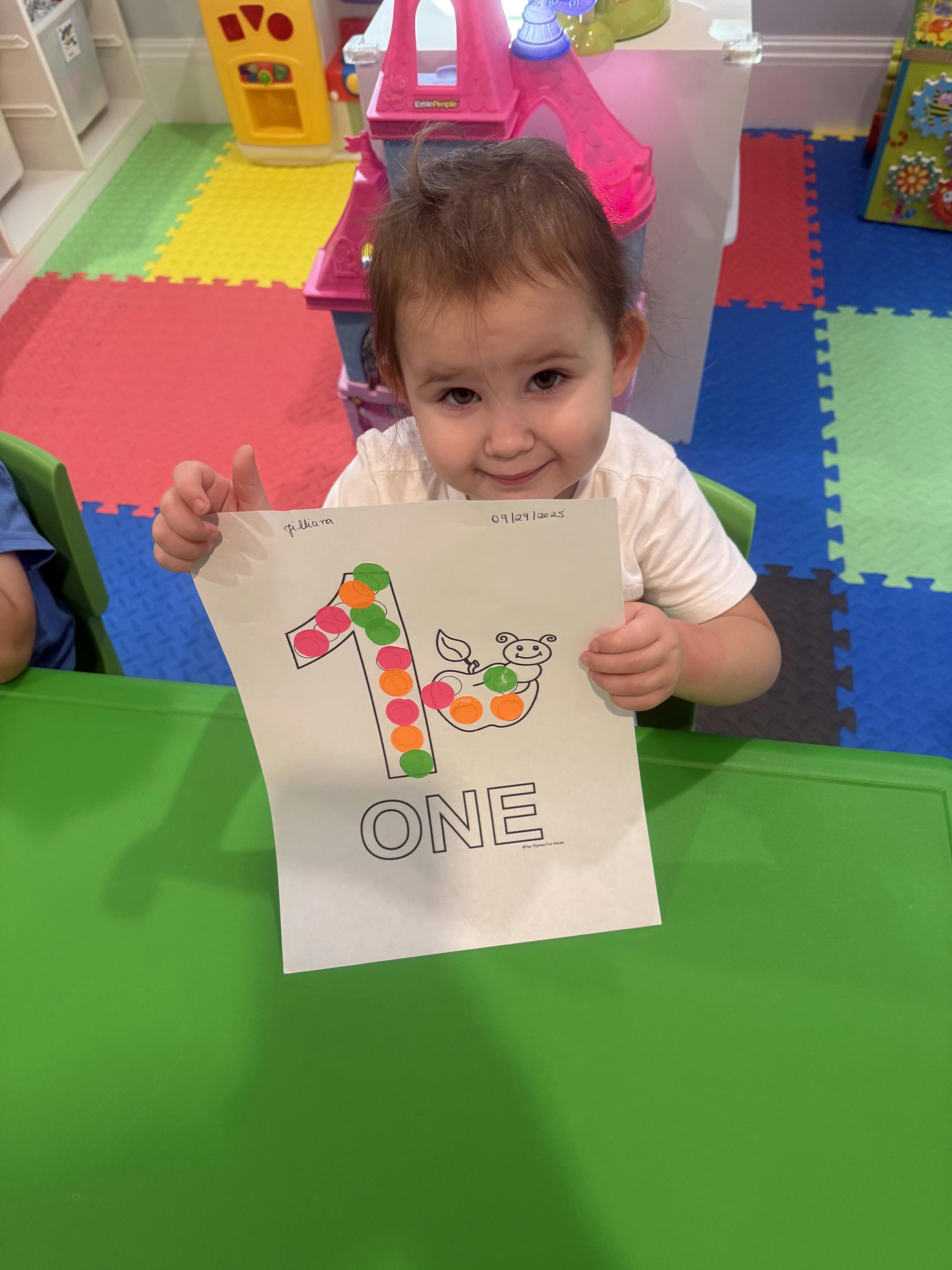 Child holding up a paper with the number one and the word ONE on it
