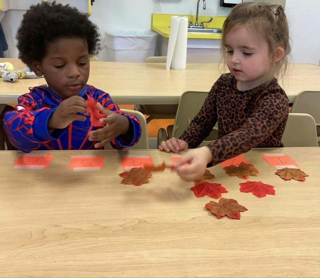 Two children counting artificial fall leaves at a table