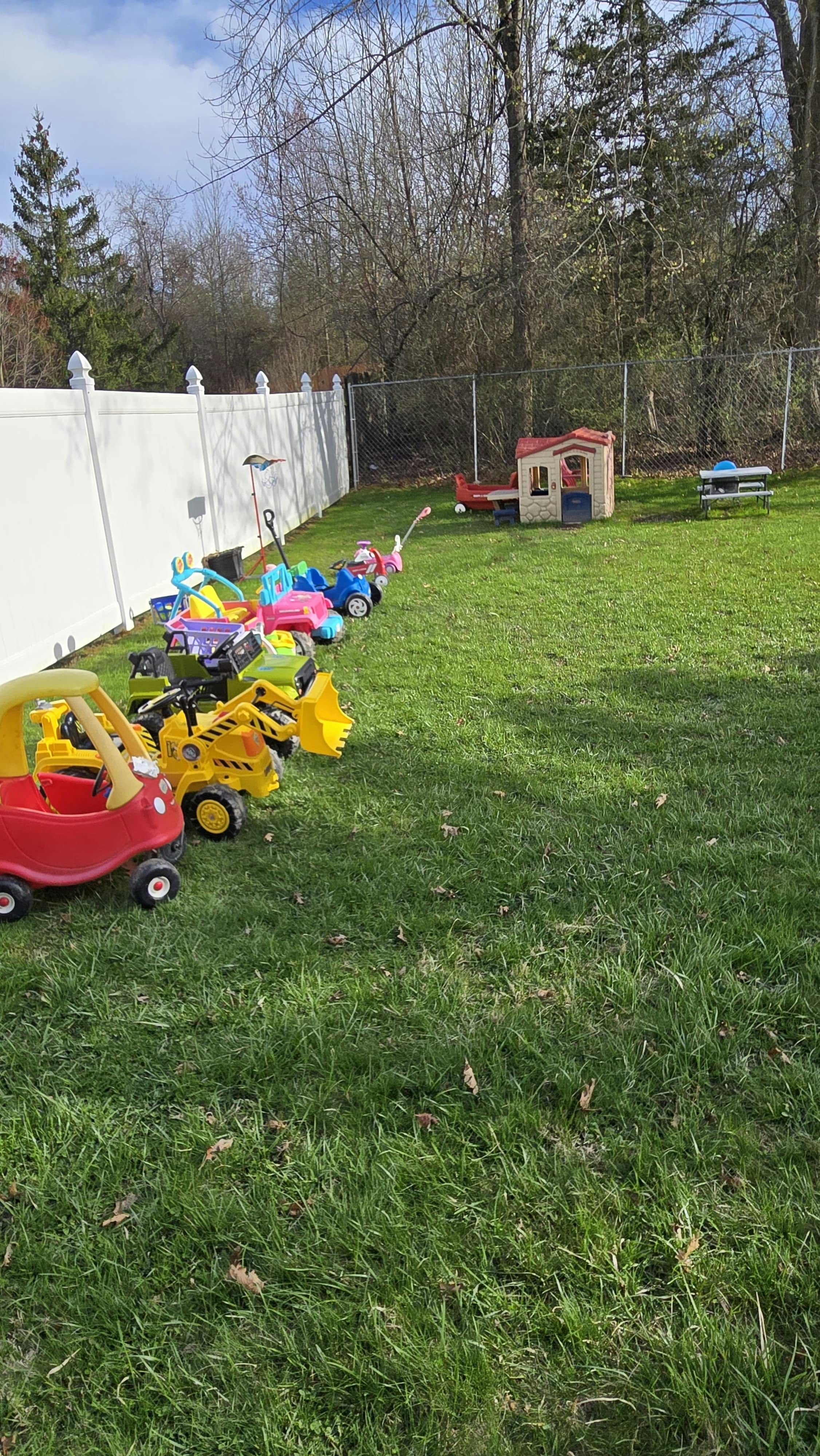 A line of children's ride-on toys and a playhouse in a grassy backyard