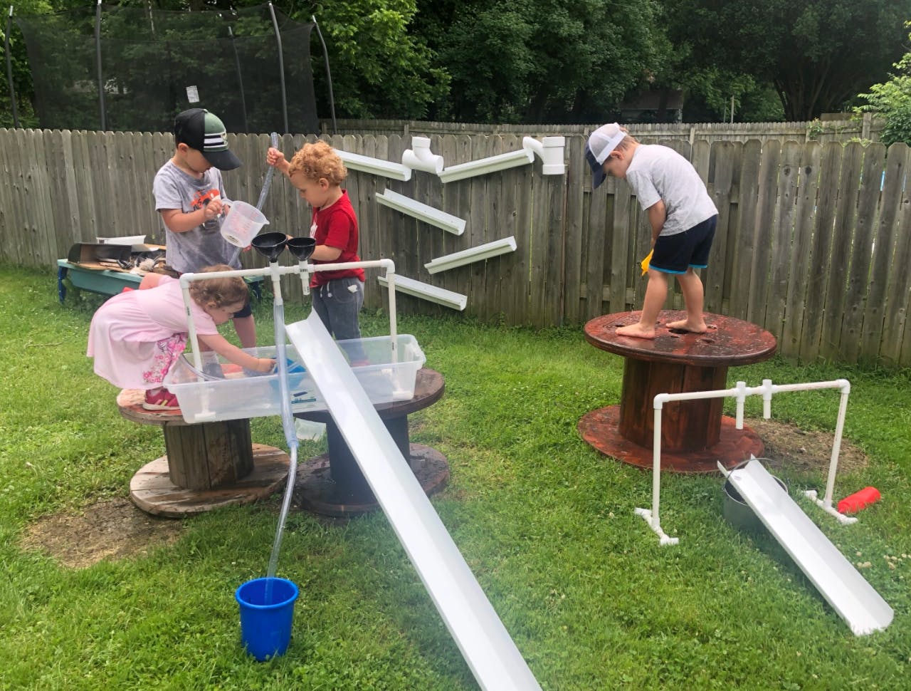 Three children playing with water and ramps in a grassy outdoor area