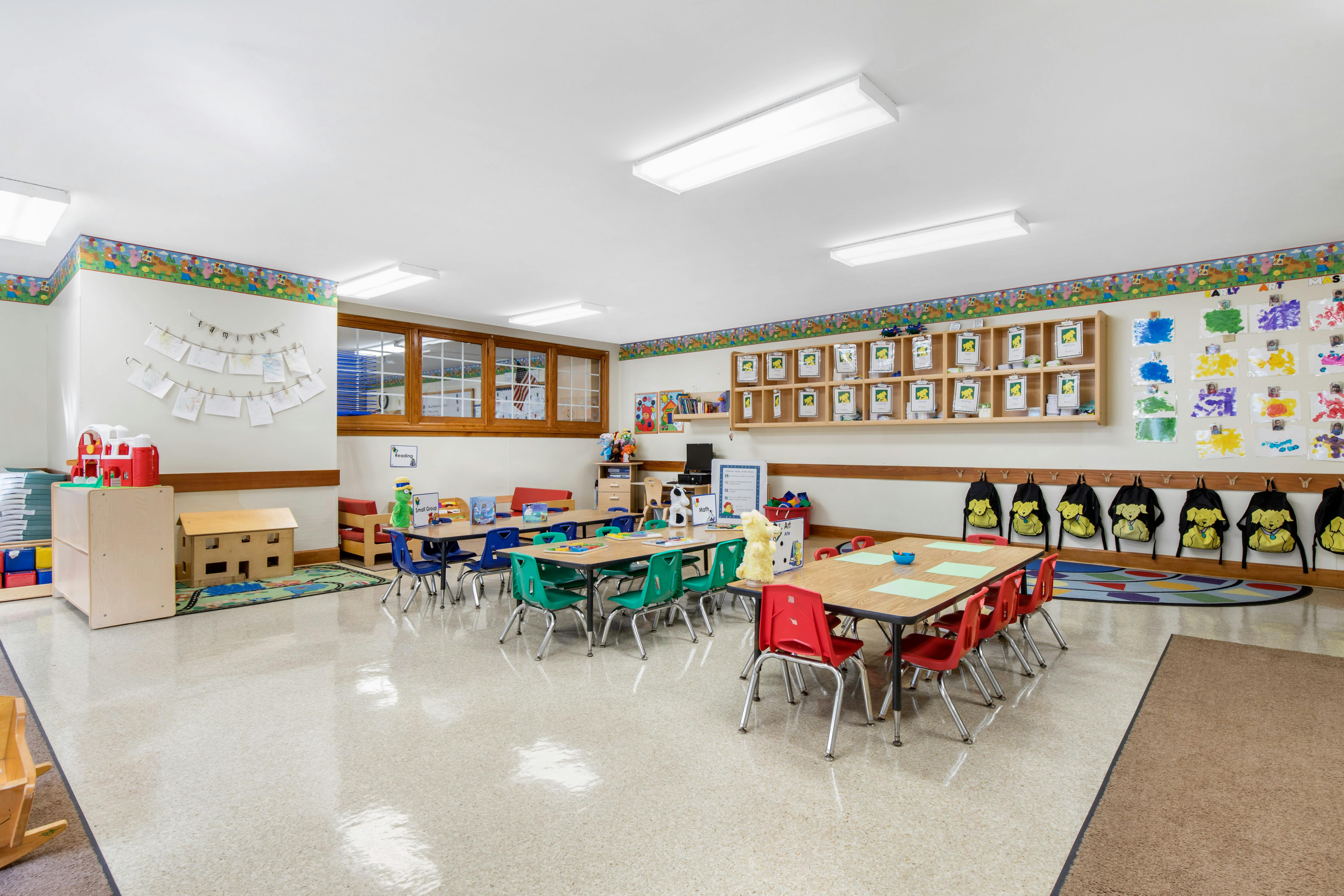 Classroom with small tables and chairs, artwork on walls, and play areas