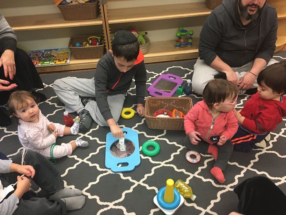 Adults and children playing with toys on a patterned rug in a classroom