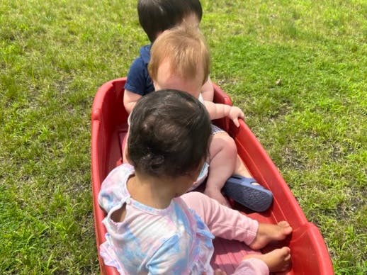 Three children sitting in a red wagon on grass