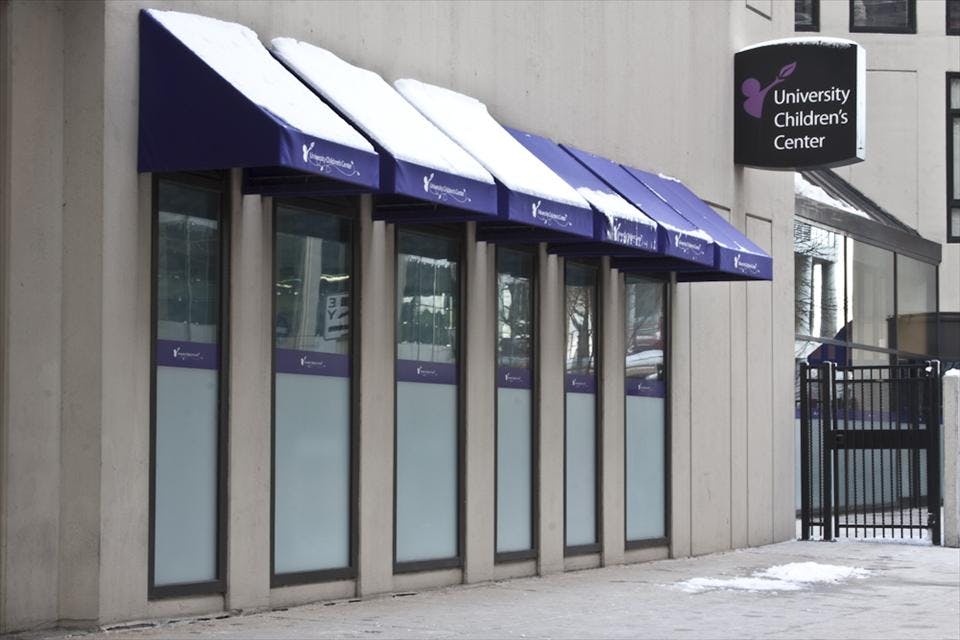Building exterior with multiple purple awnings covered in snow, sign "University Children's Center"