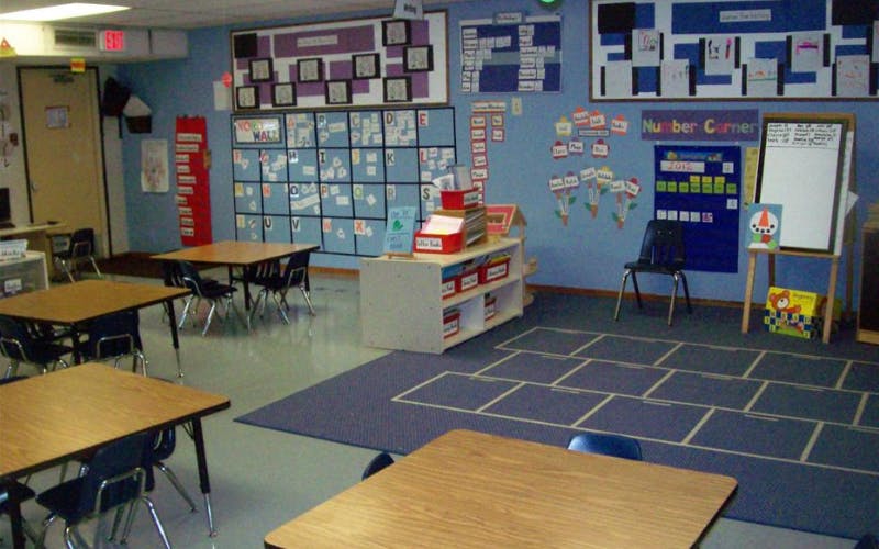 An empty classroom with small tables and chairs, a number corner, and alphabet board
