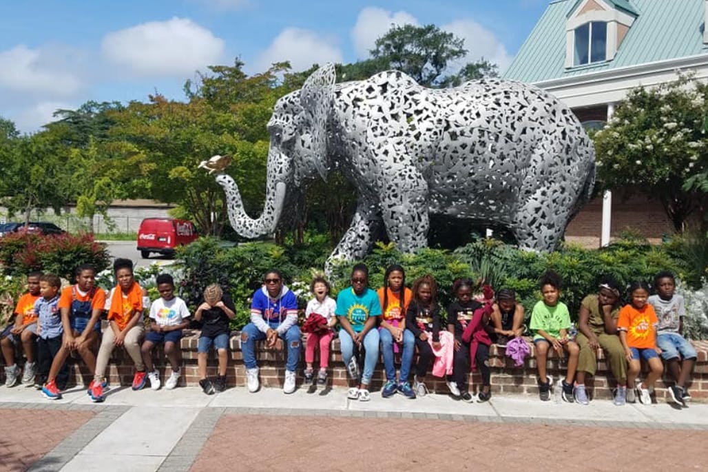 Group of people and children sitting in front of an elephant sculpture