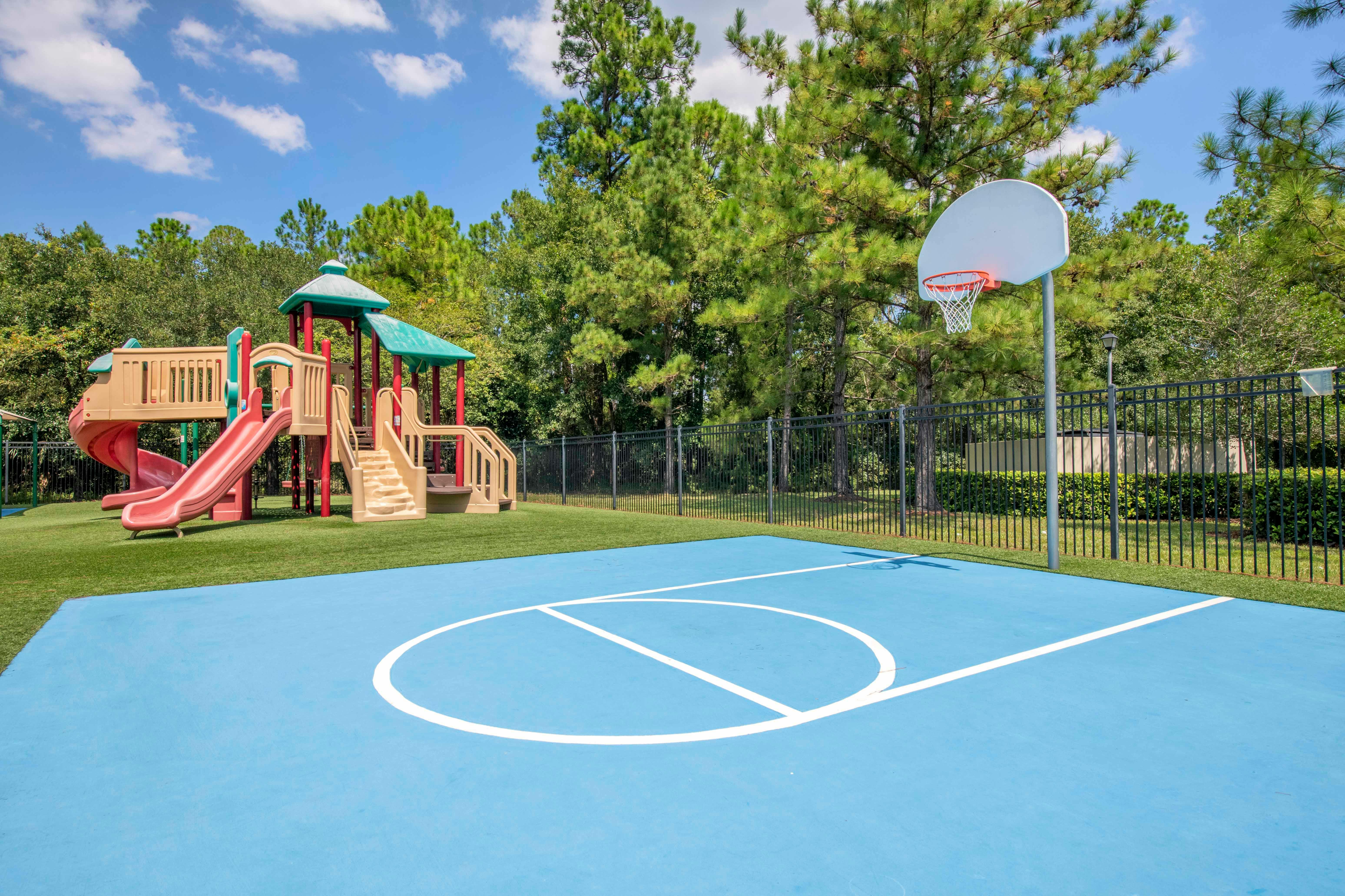 A blue basketball court with white lines next to a playground with slides