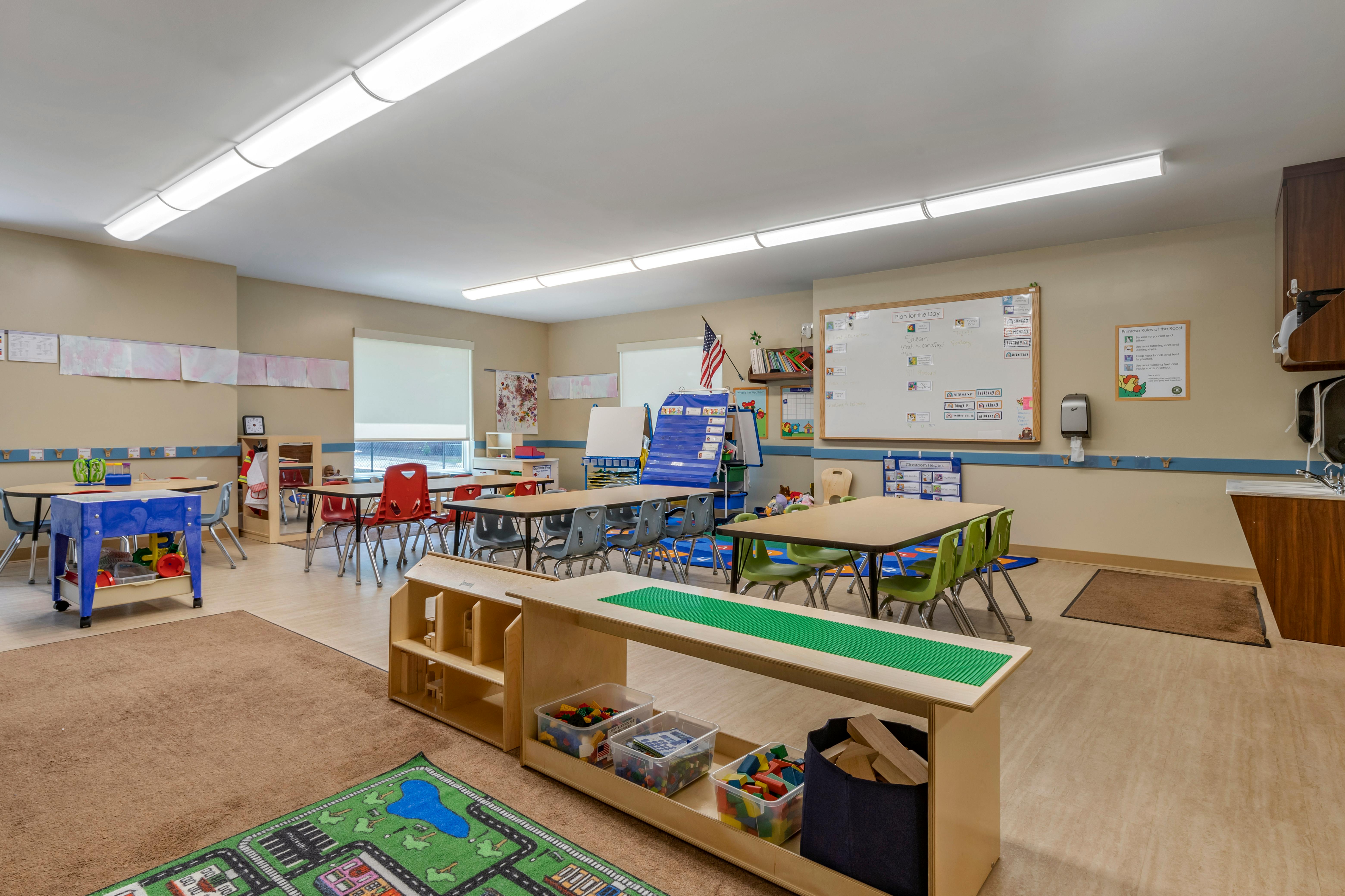 An empty classroom with small tables and chairs, and play equipment