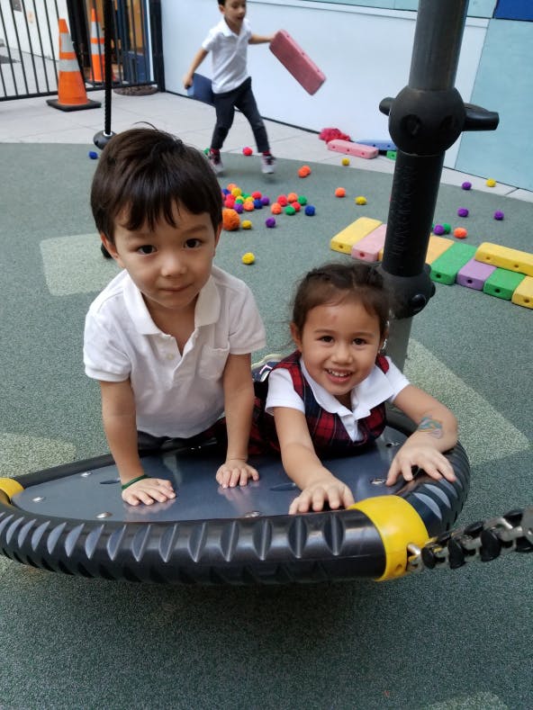 Two children on a playground spinner, another child in background