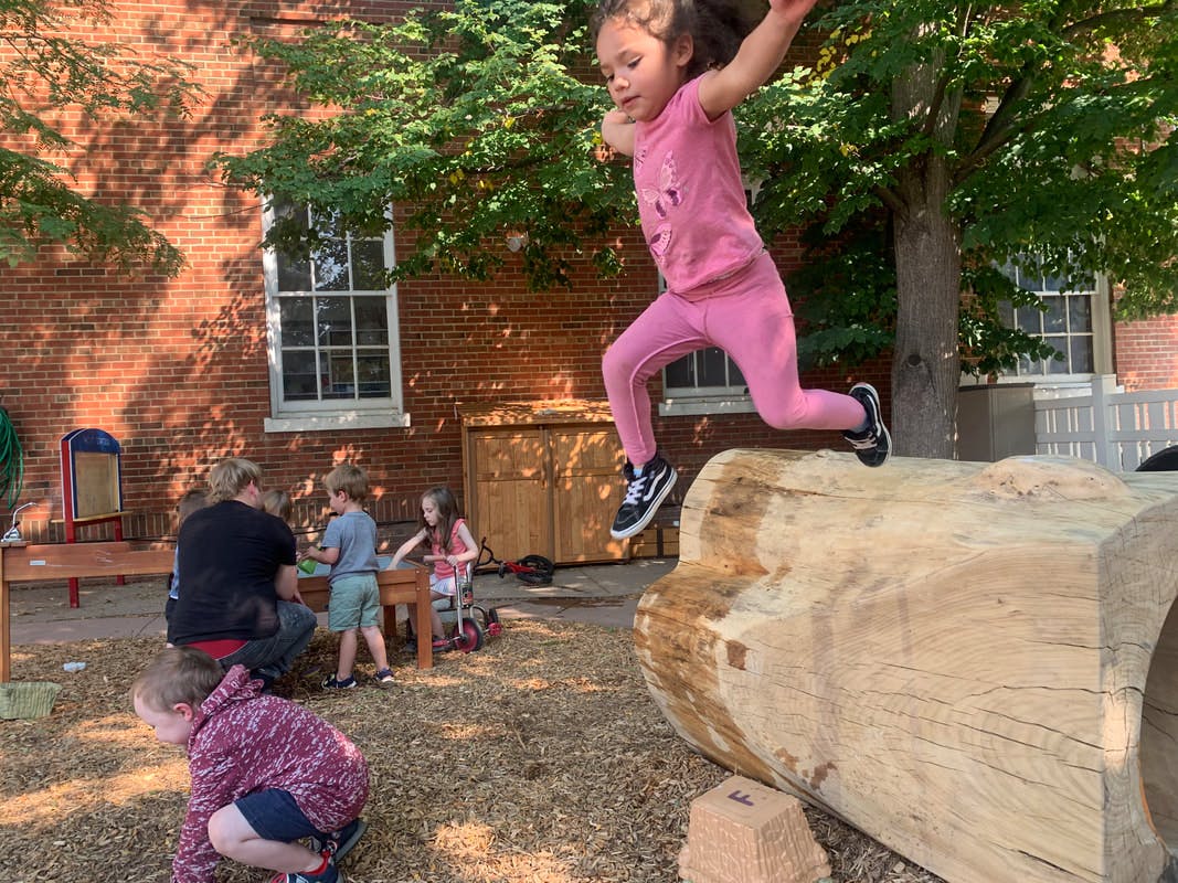 Child jumping over a large log on a playground