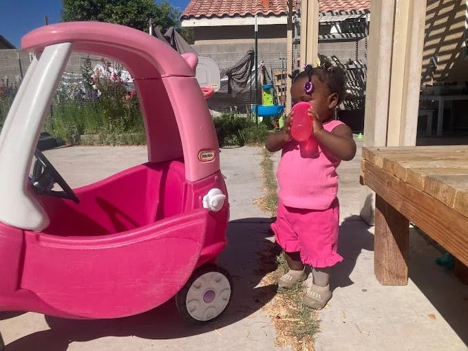 Child standing by a plastic toy car and drinking from a cup