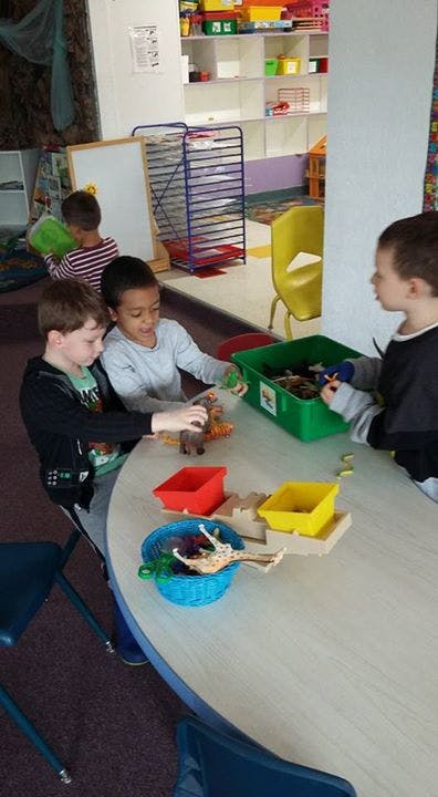 Three children playing with toys at a table in a classroom