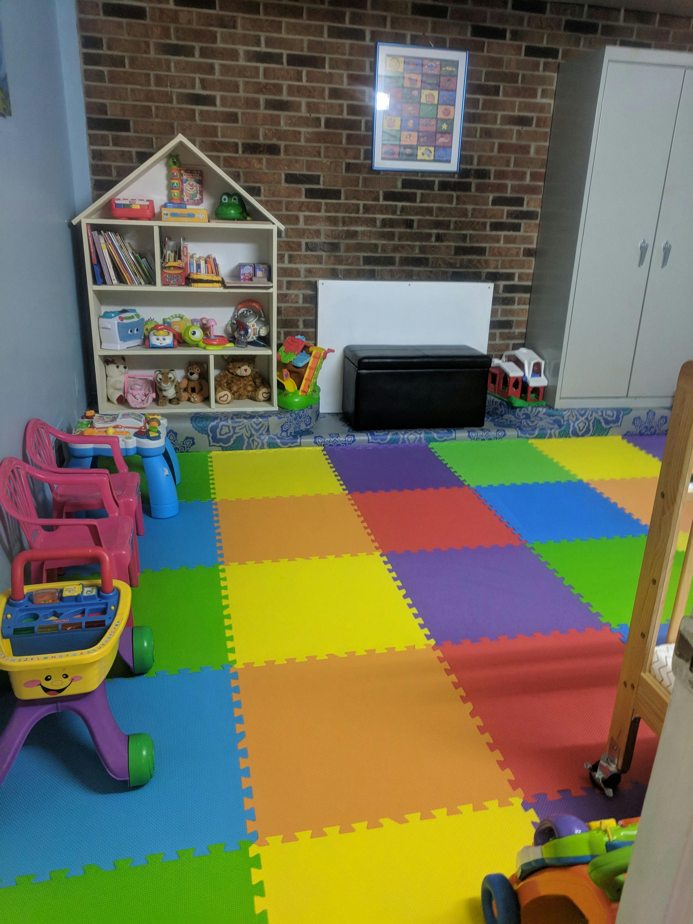 Playroom with colorful floor mats, toy shelf, and small chairs