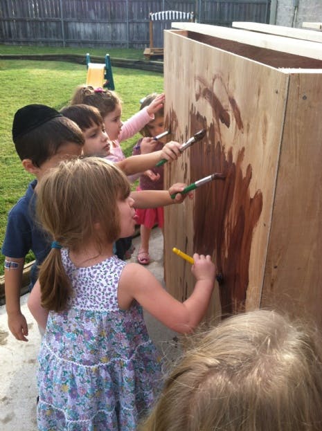 Children painting on a wooden surface outdoors