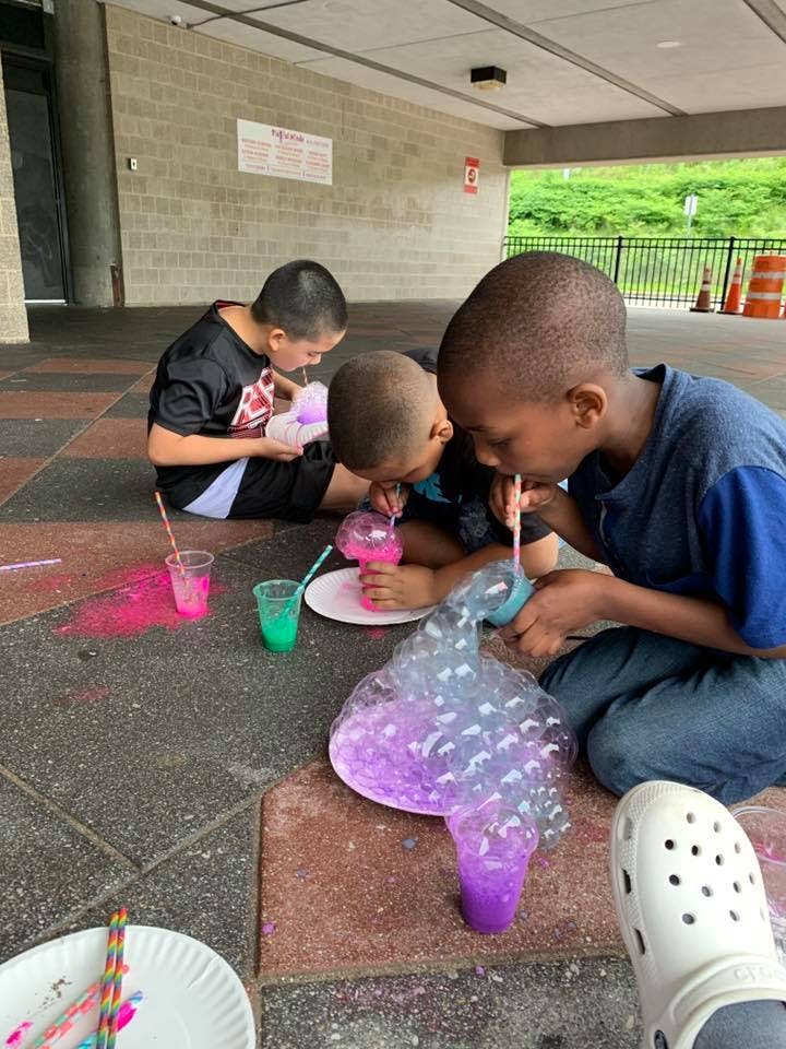 Three children blowing bubbles with straws into colorful liquid