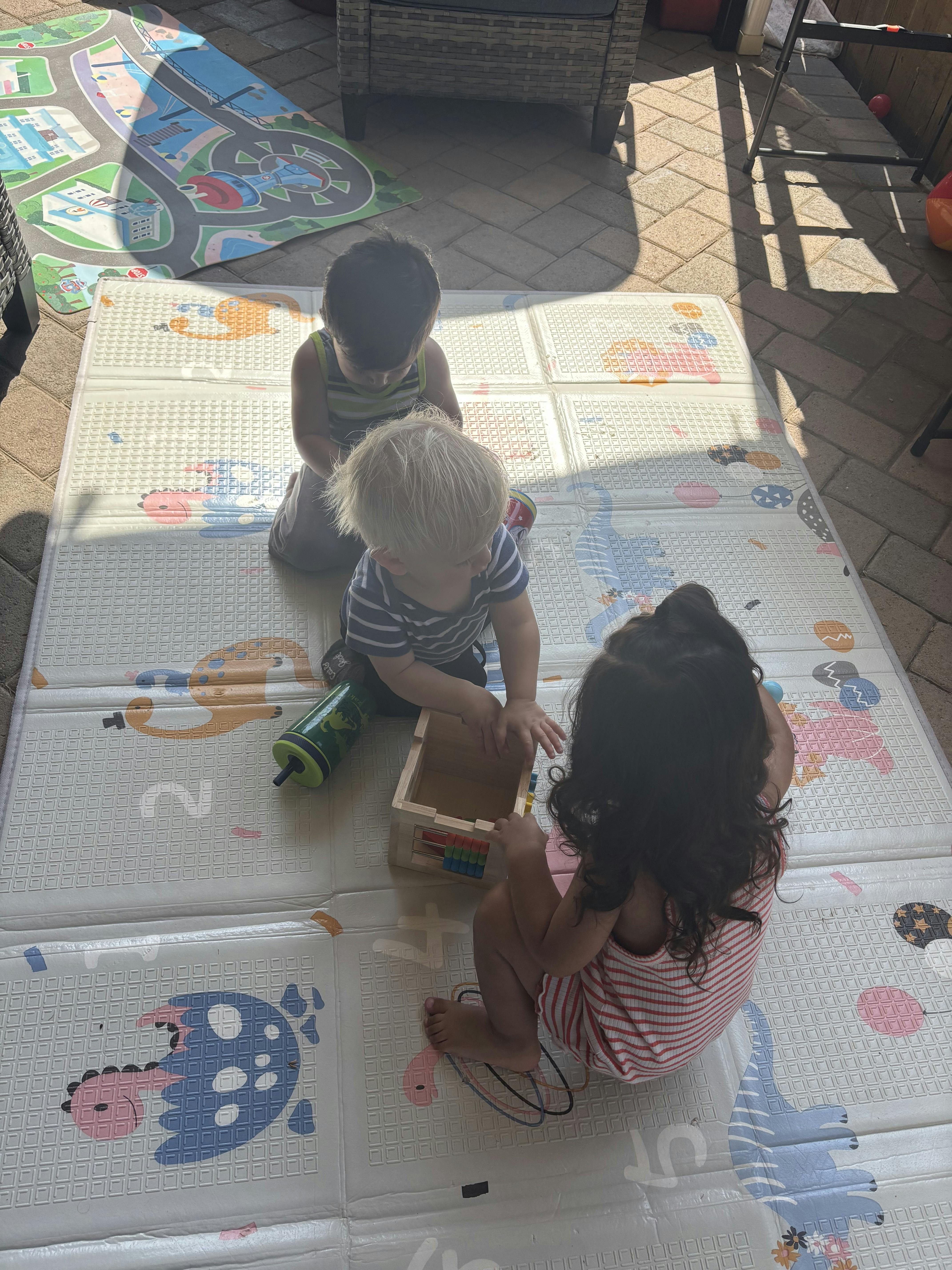 Three children playing on a mat outdoors