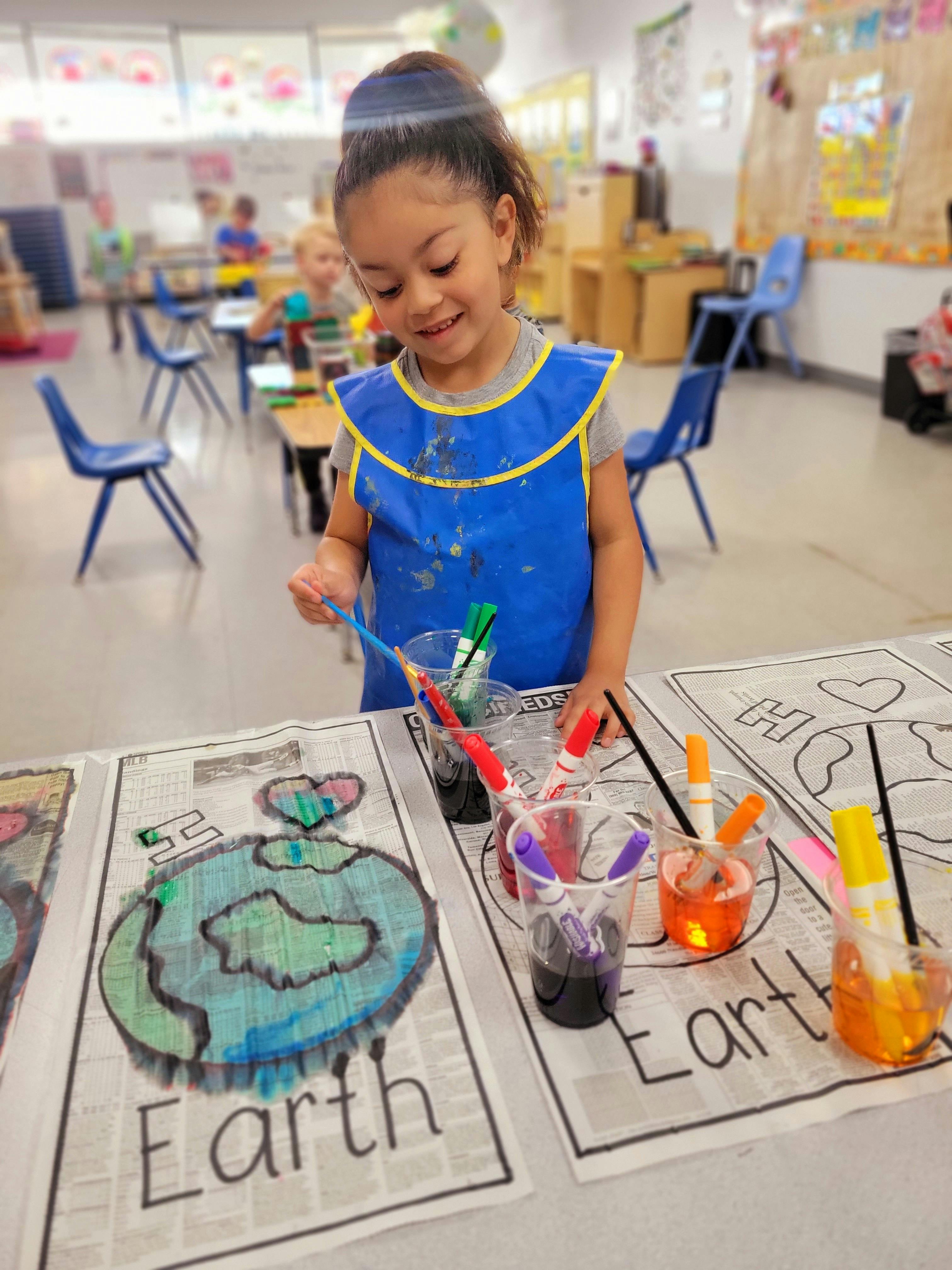 Child in a blue smock painting a picture of Earth