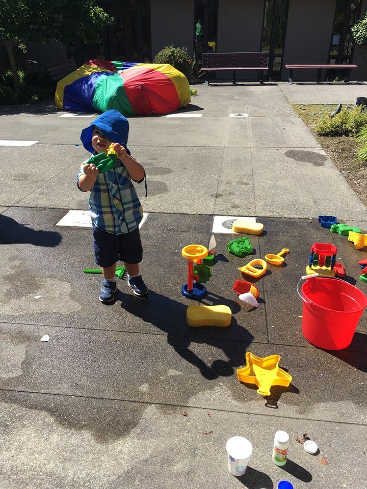 Child in a blue hat playing with toys on a paved surface outdoors area