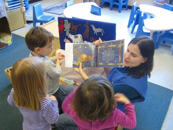 Person reading a book to three children in a classroom