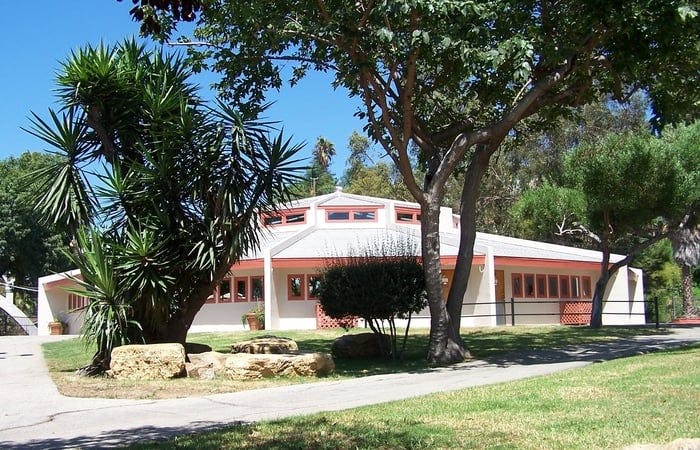 Building with a white roof and light-colored walls surrounded by trees and grass