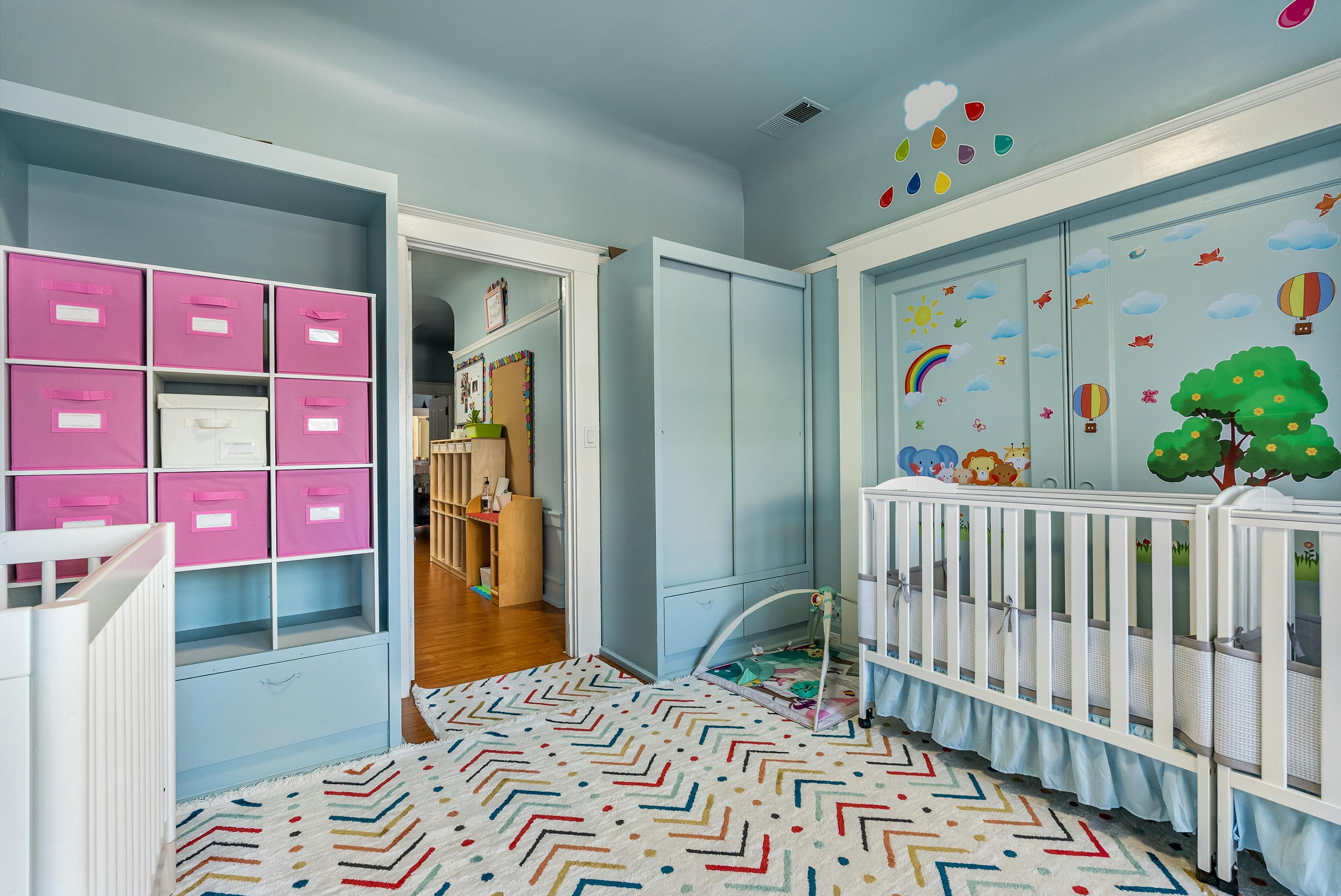 Nursery room with two cribs and storage shelves with pink bins