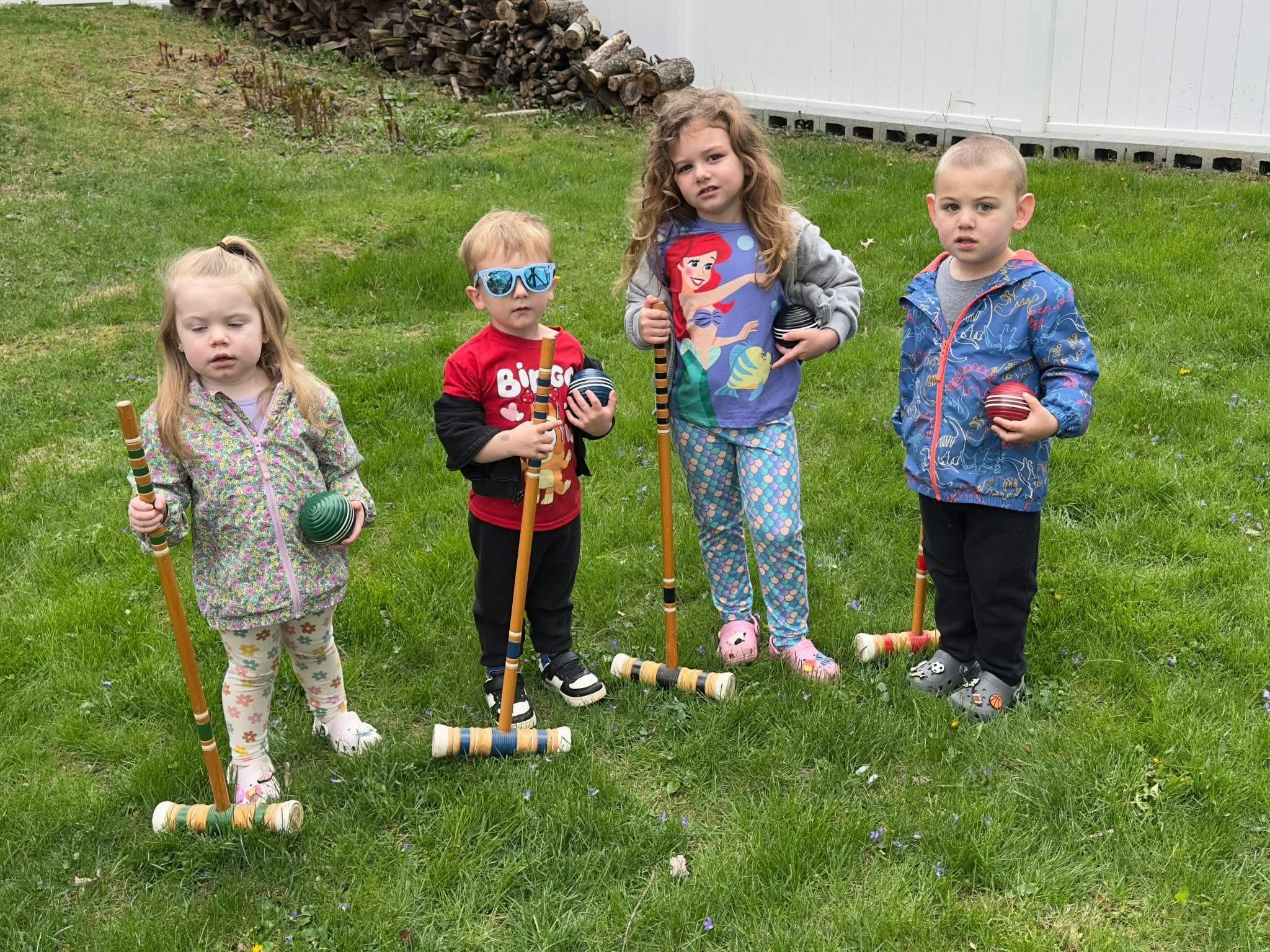 Four children standing on grass with croquet mallets and balls
