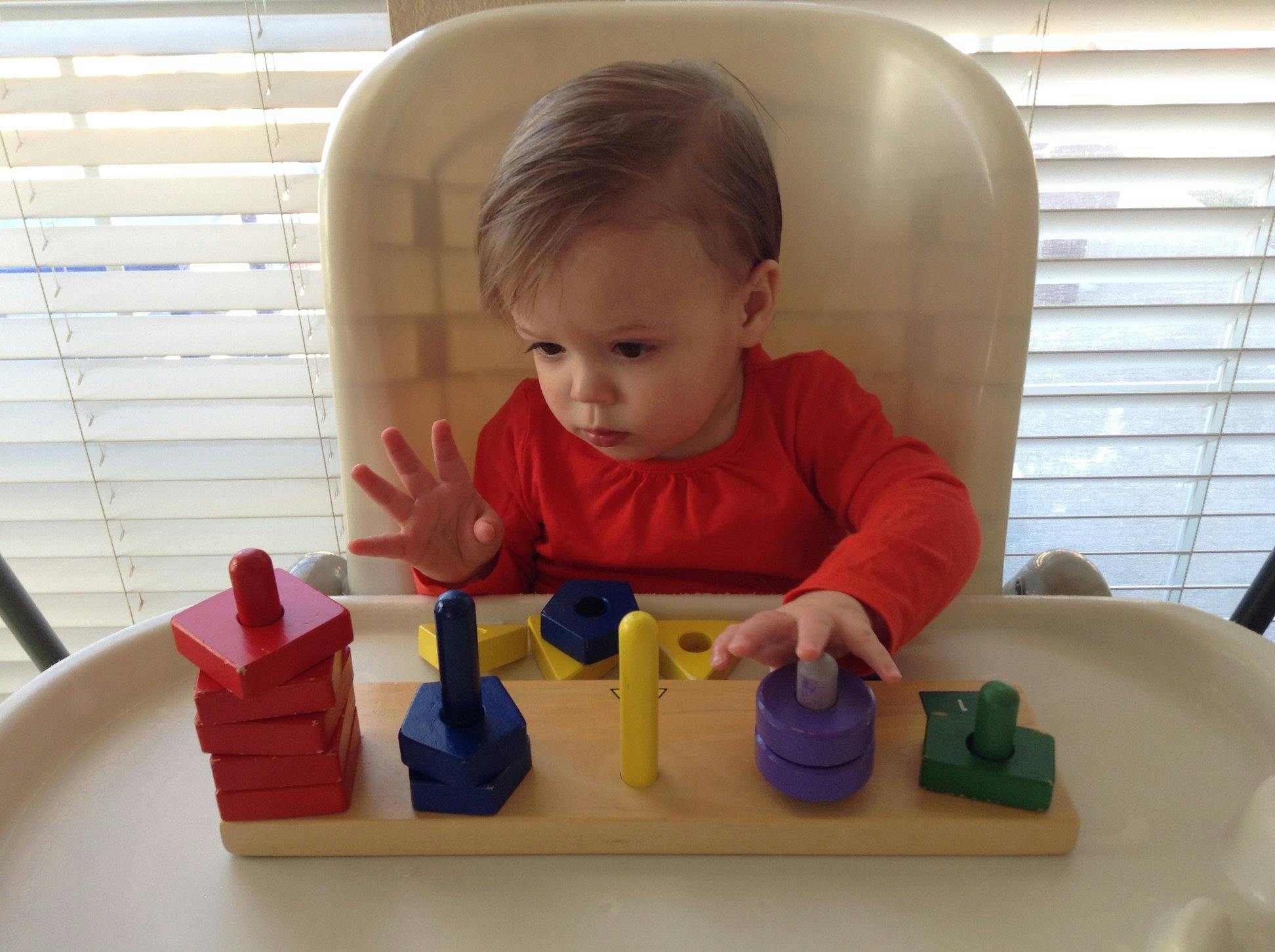 Child in a high chair playing with a wooden shape sorter toy