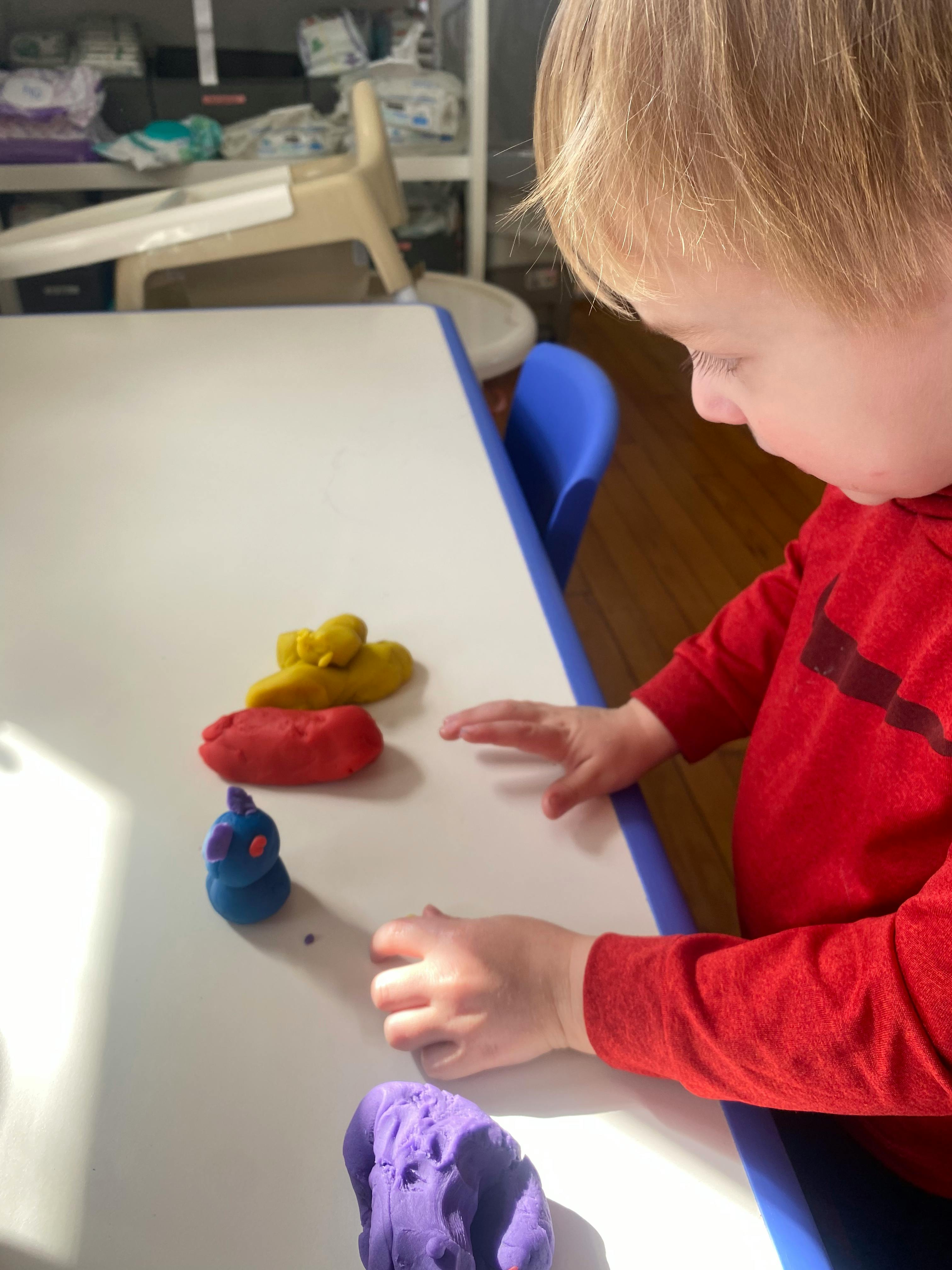 Child playing with colorful playdough on a white table