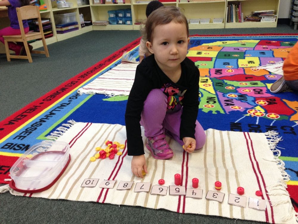 Child playing with number tiles and red pegs on a striped mat