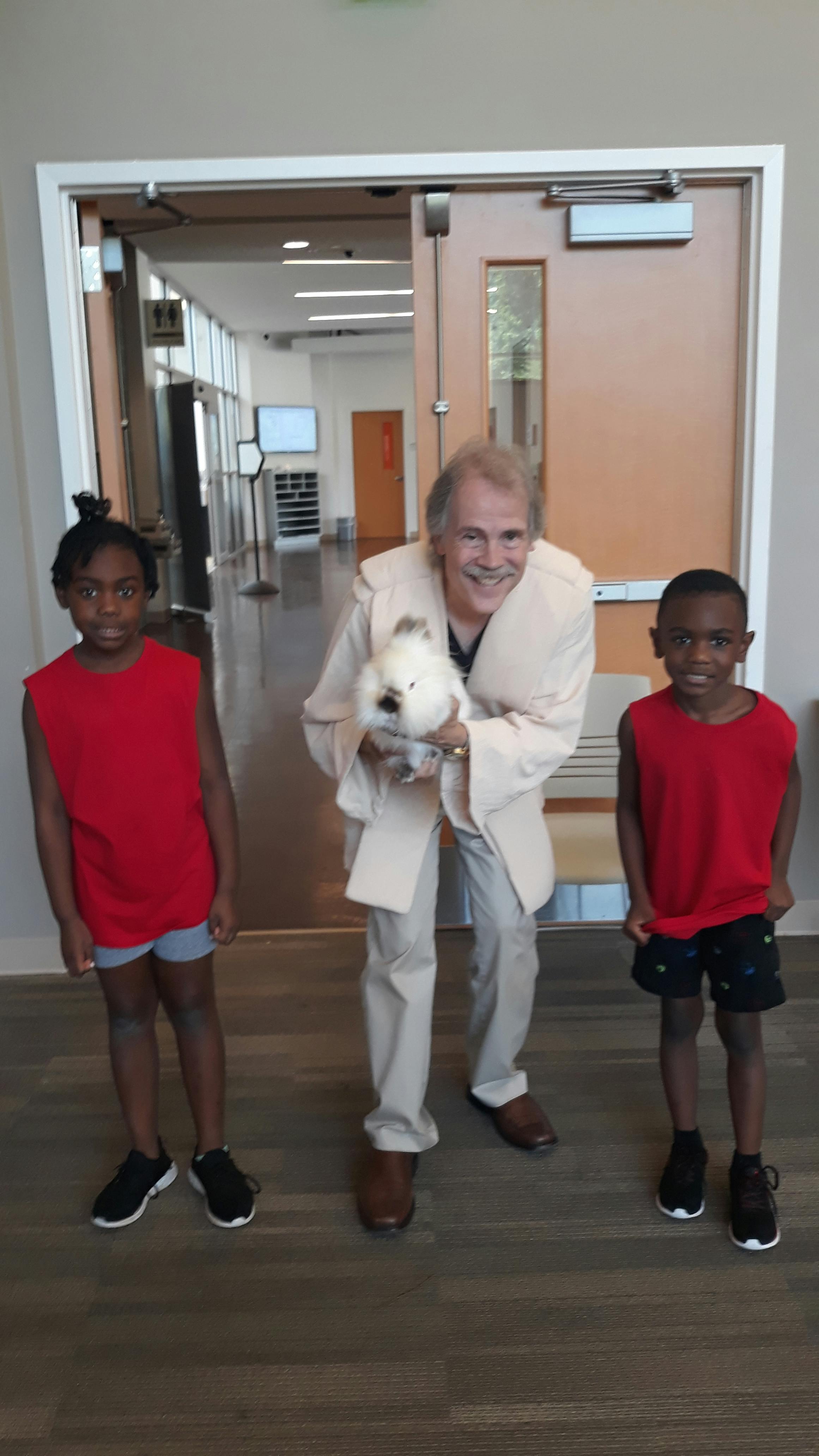 Adult holding a white stuffed animal with two children standing nearby
