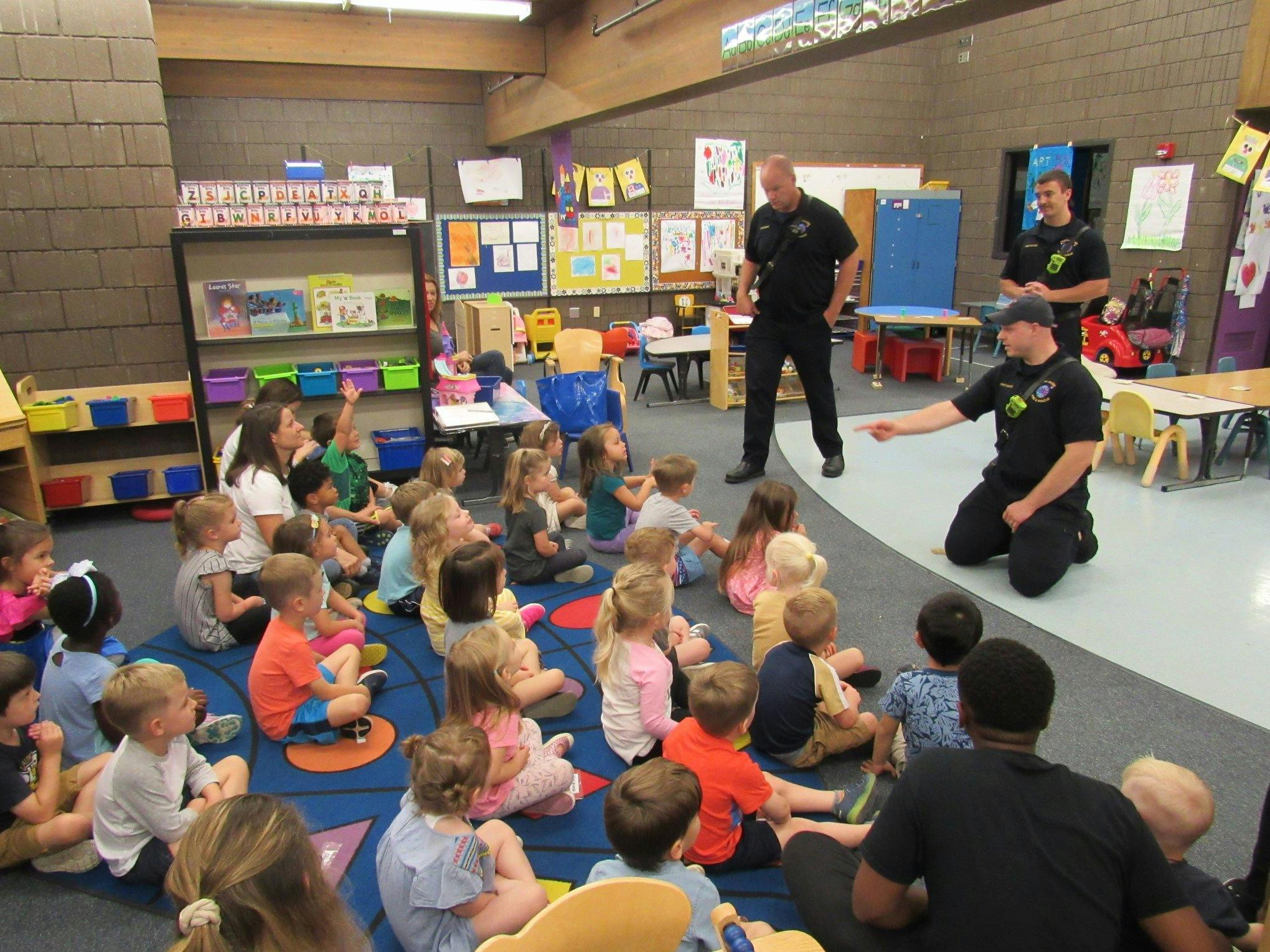 Adults in uniform speaking to a group of children in a classroom