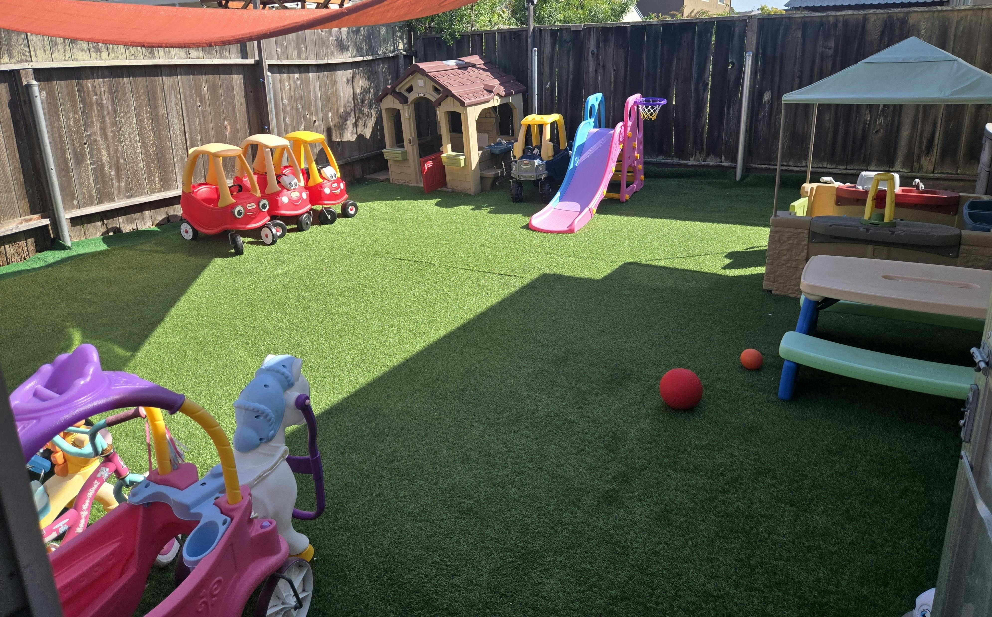 Playground with toy cars, playhouse, slide, and picnic table on artificial grass