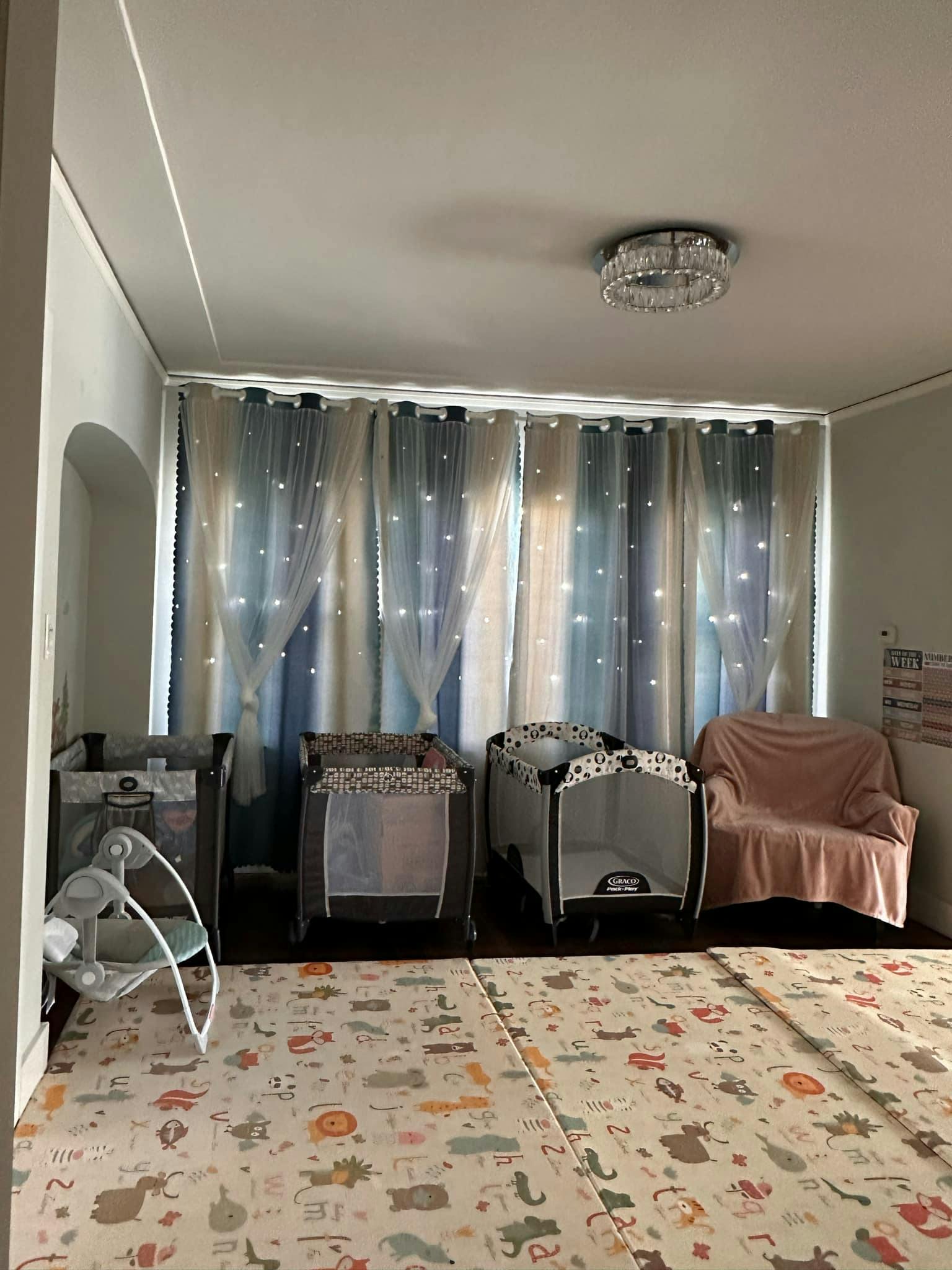 Three playards and a baby swing in a room with a patterned floor mat