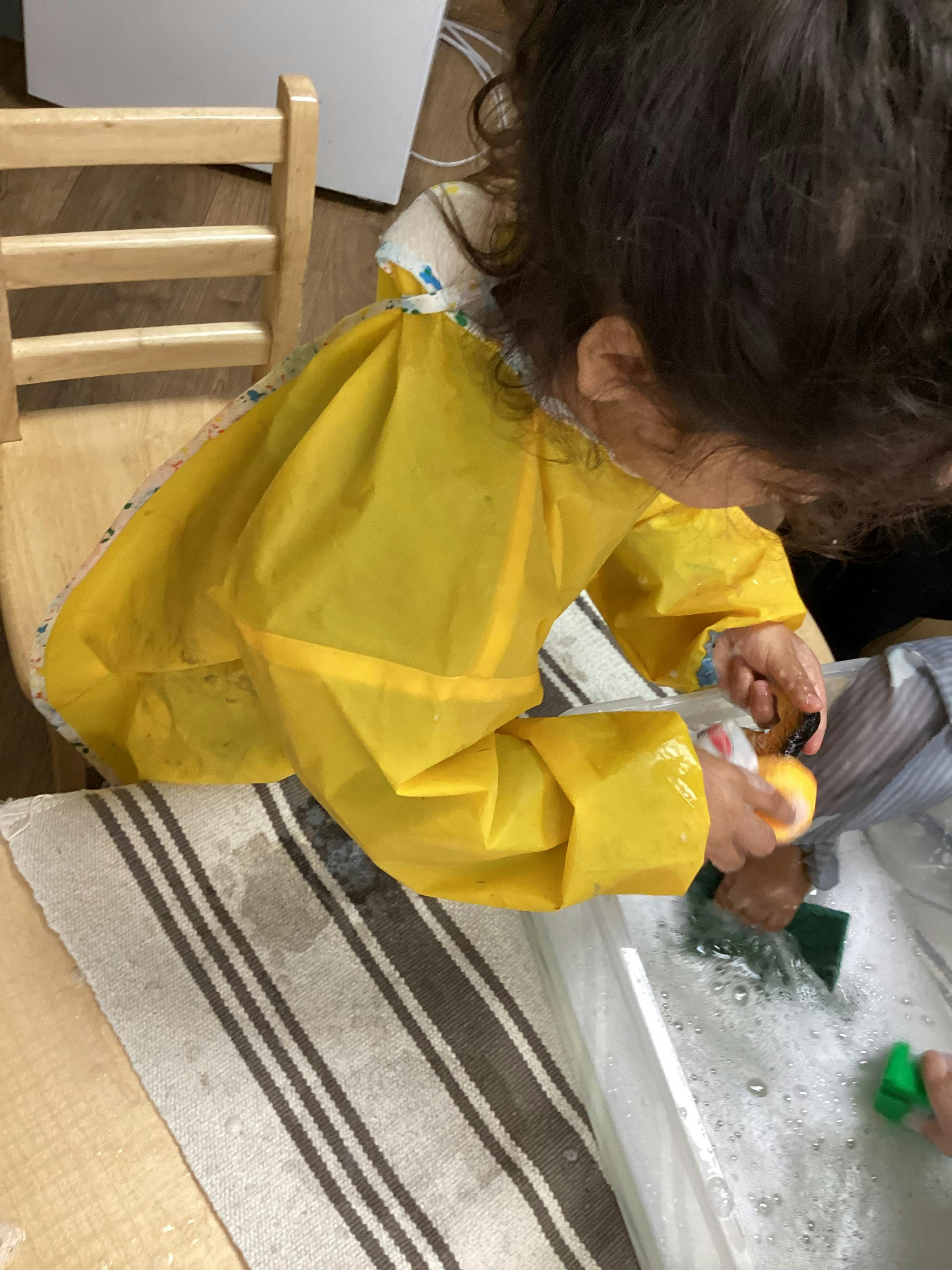 Child in yellow smock washing items in a tub of soapy water
