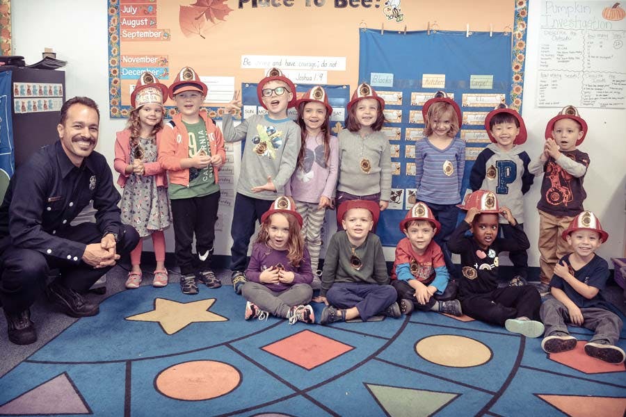Person and children wearing firefighter hats in a classroom