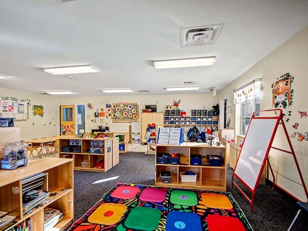 A colorful classroom with a whiteboard, tables, and storage shelves