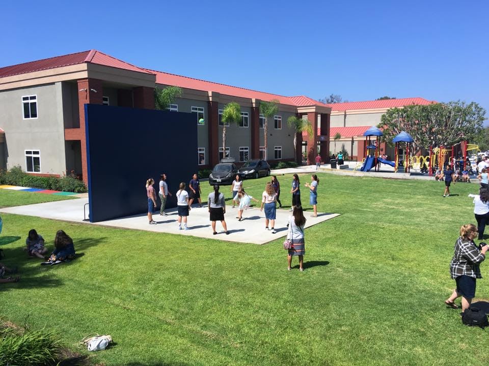 People gathered on a lawn in front of a building with a playground inky blue wall