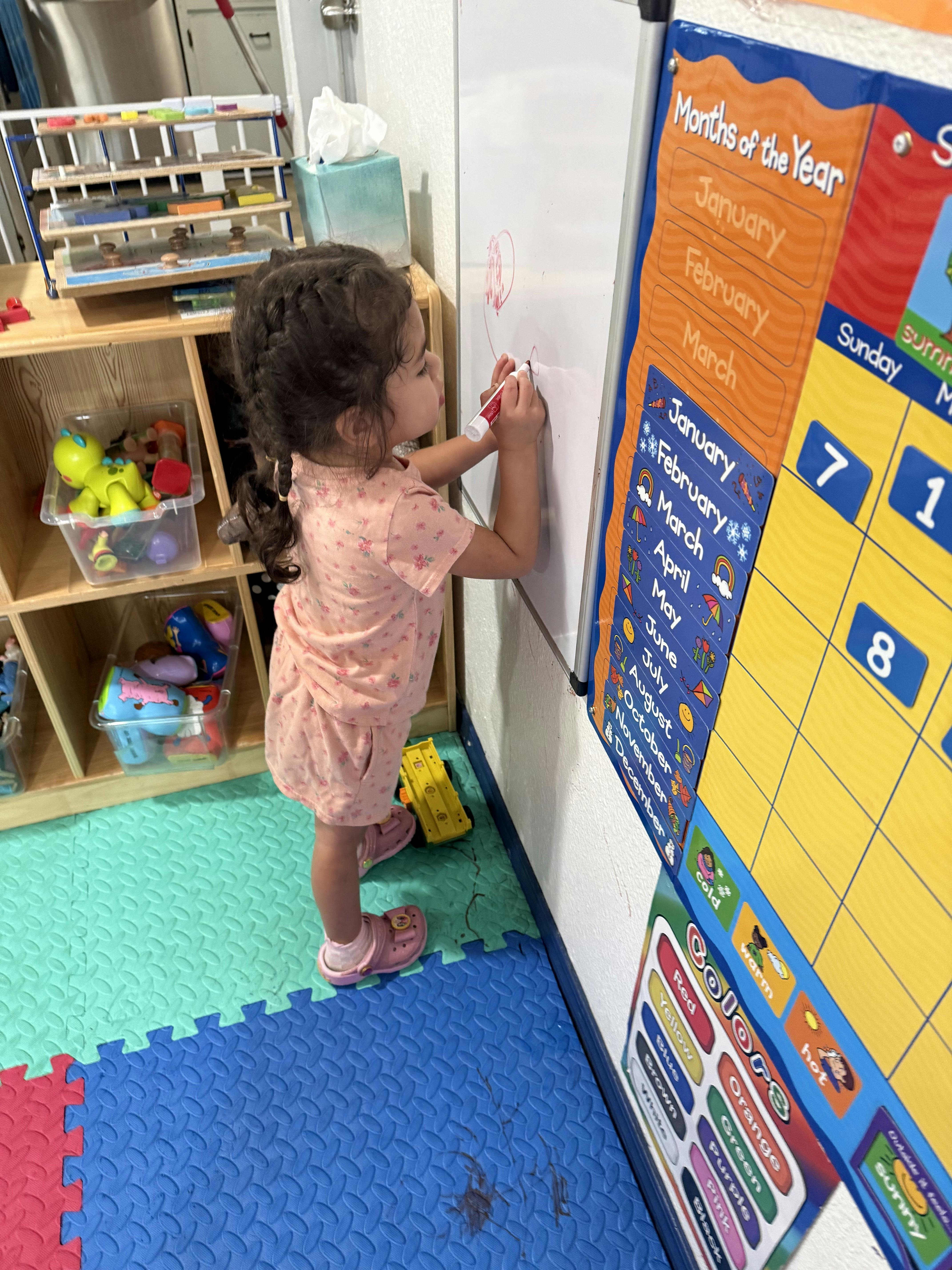 Child drawing with a marker on a whiteboard in a classroom
