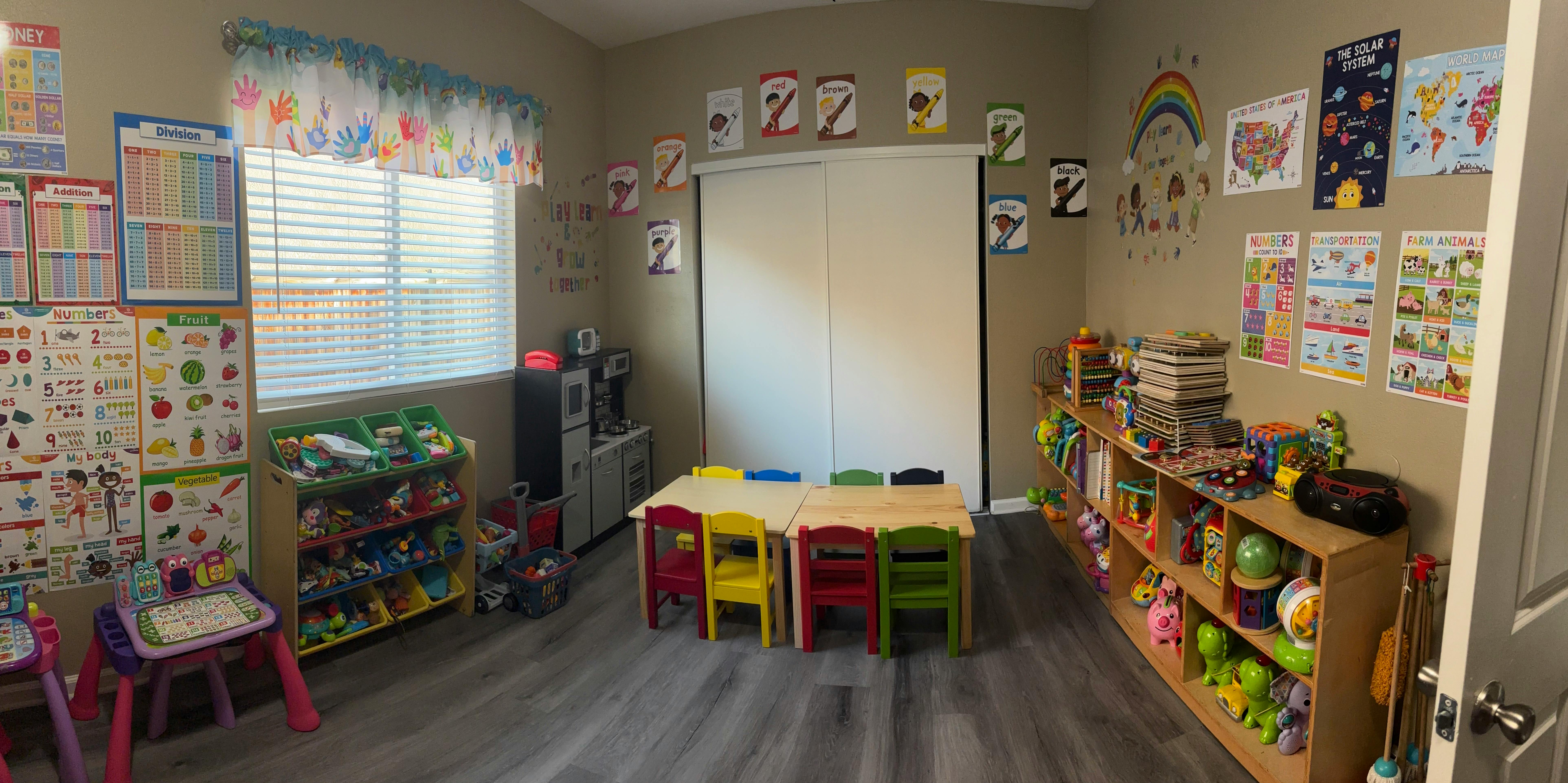 A colorful classroom with a children's kitchen, tables and chairs, and shelves of toys