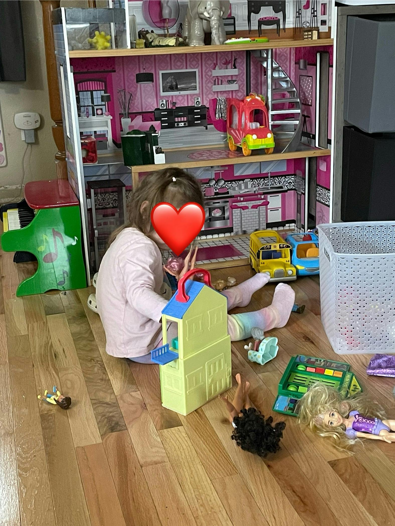 Child playing with dolls and a dollhouse on a wooden floor