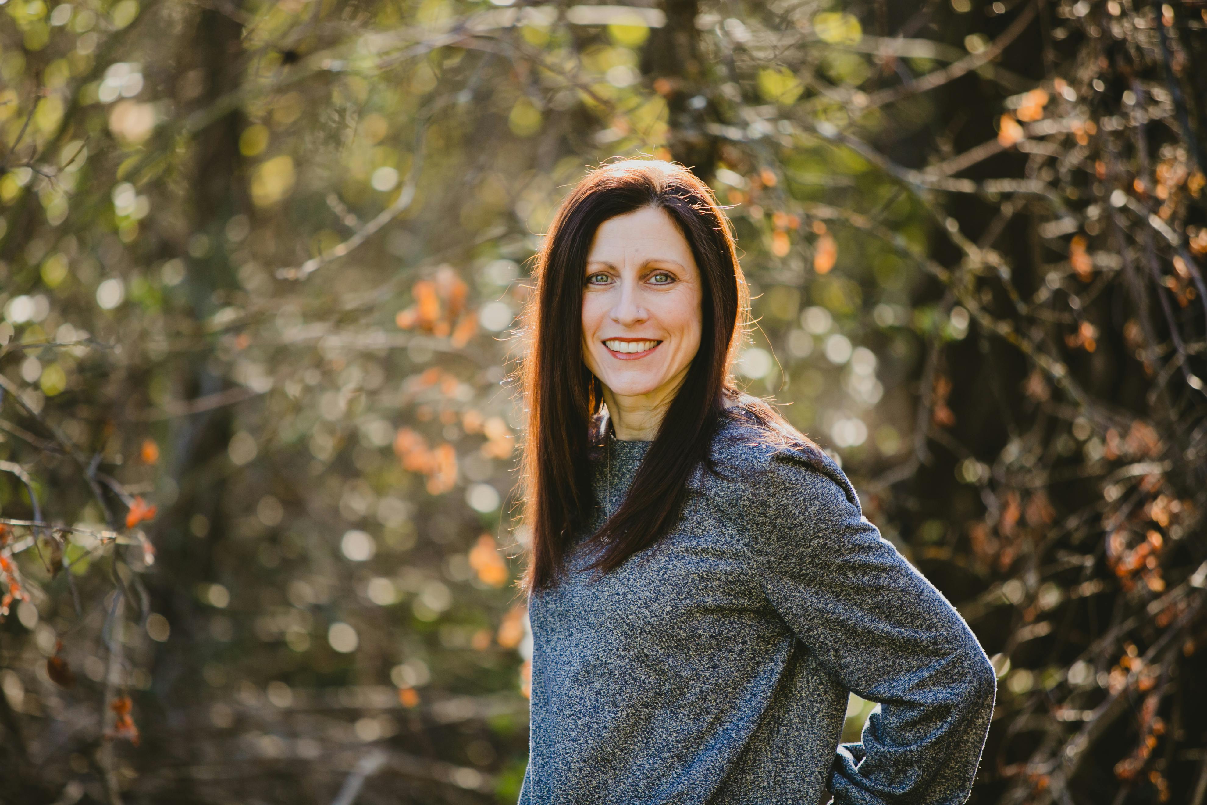 Smiling person with long hair against a blurred natural background