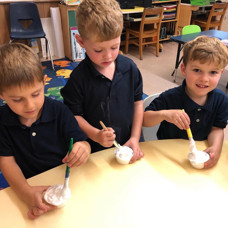 Three children at a table with cups and brushes