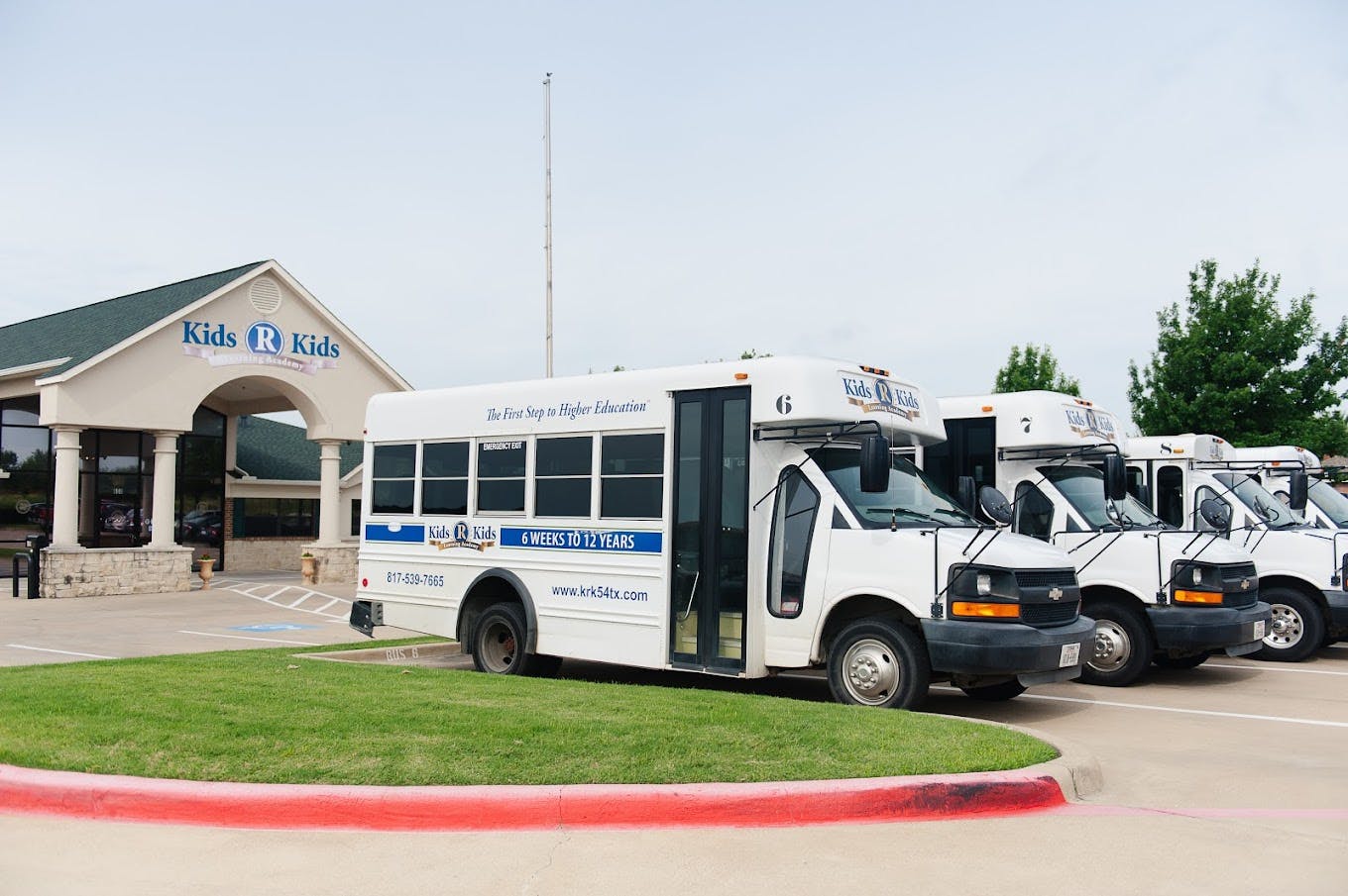 White shuttle buses parked outside a building with "Kids R Kids Learning Academy" on it