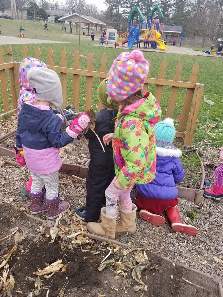 Children playing in a garden bed with a playground in the background