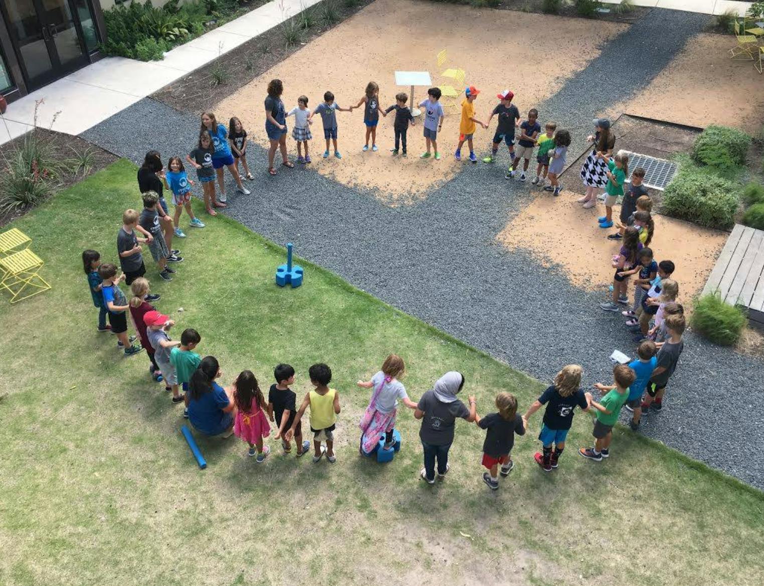 Group of children and adults holding hands in a large circle outdoors