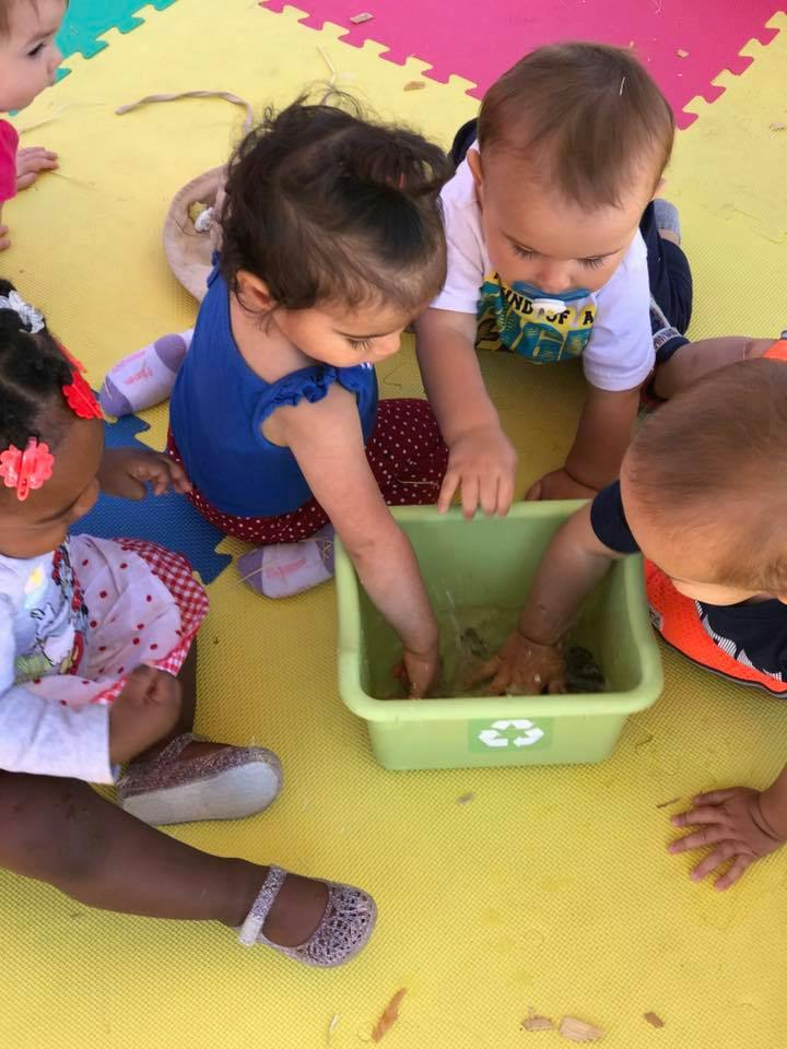 Children playing with water in a green bin on a yellow mat