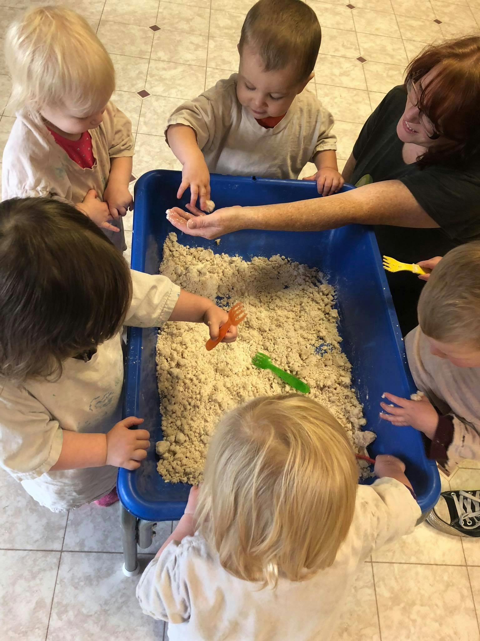Children playing with sand in a blue bin